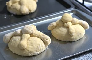 Bolas de masa de pan de muerto con las tiras de 'huesos' encima, listas para hornear.
