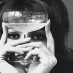 Mujer sosteniendo una copa de cristal frente a los ojos en una fotografía antigua en blanco y negro, el sabor y el flavor