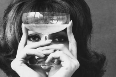 Mujer sosteniendo una copa de cristal frente a los ojos en una fotografía antigua en blanco y negro, el sabor y el flavor