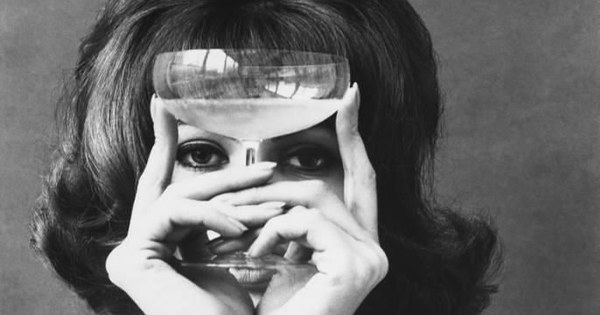 Mujer sosteniendo una copa de cristal frente a los ojos en una fotografía antigua en blanco y negro, el sabor y el flavor